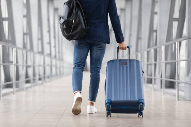 Unrecognizable Man With travel Bag And Suitcase Walking In Airport Terminal.