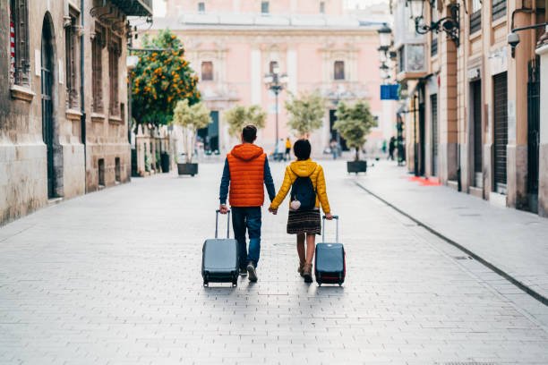 Man and woman going to trip while holding the hand of each other and holding their travel bangs with them.